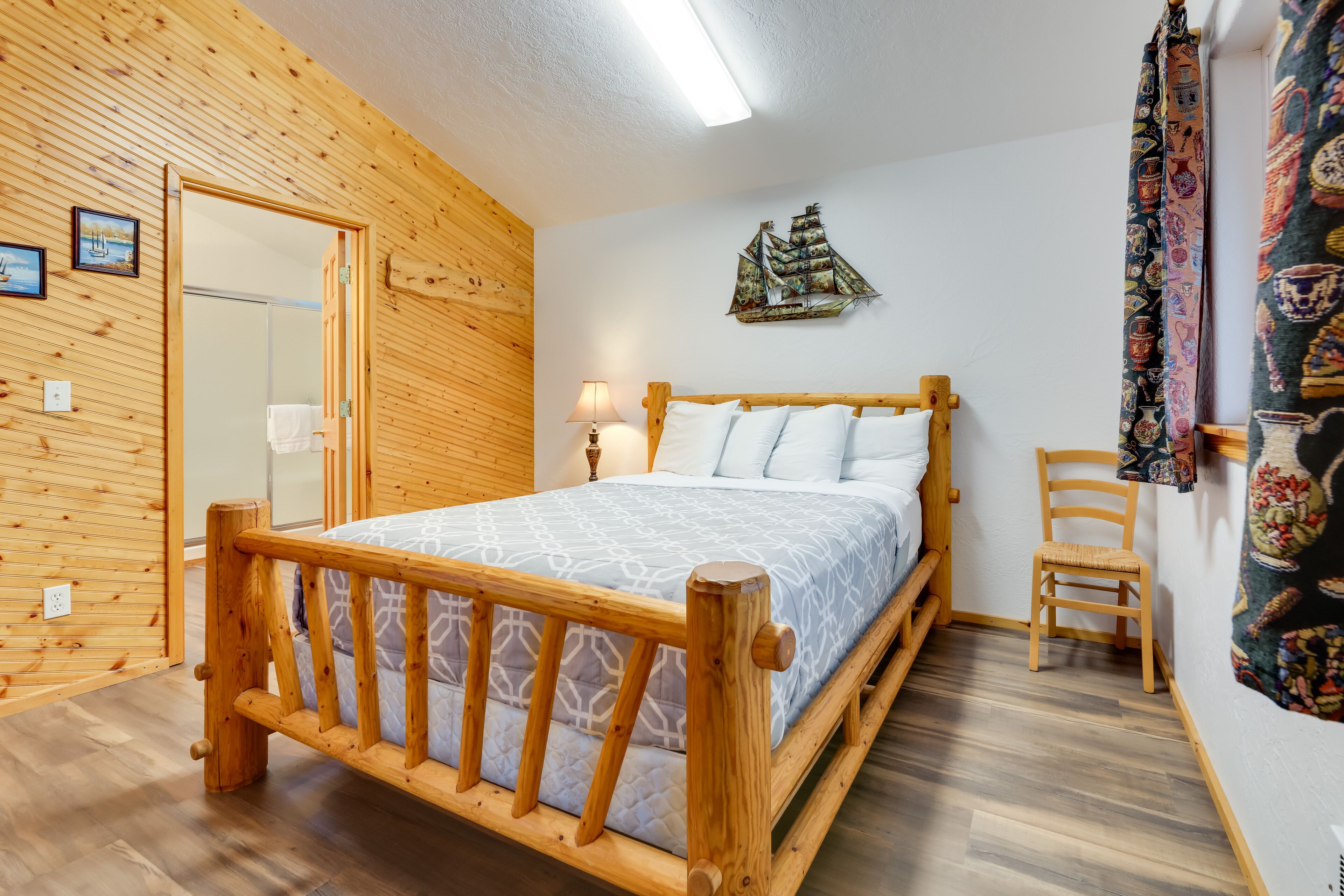 A wooden-framed bed with a patterned bedspread, a small wooden chair, and a wall-mounted ship decoration.