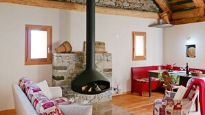 Un salon rustique avec une cheminée en pierre, des poutres en bois et un coin repas aux couleurs rouge.