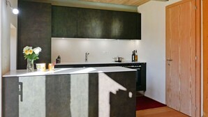 Une cuisine moderne dotée d’un îlot central, de meubles de rangement aux couleurs sombres et d’une porte en bois.