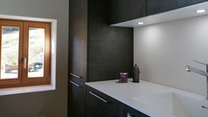 Une cuisine moderne avec des meubles de couleur sombre, un plan de travail blanc et une fenêtre donnant sur l’extérieur.