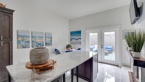 A modern kitchen with a marble countertop, a wooden bowl, and a dining area with blue chairs.