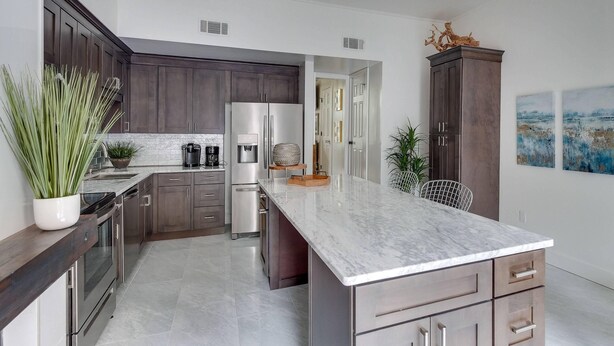 A modern kitchen with dark wood cabinets, stainless steel appliances, and a marble countertop.