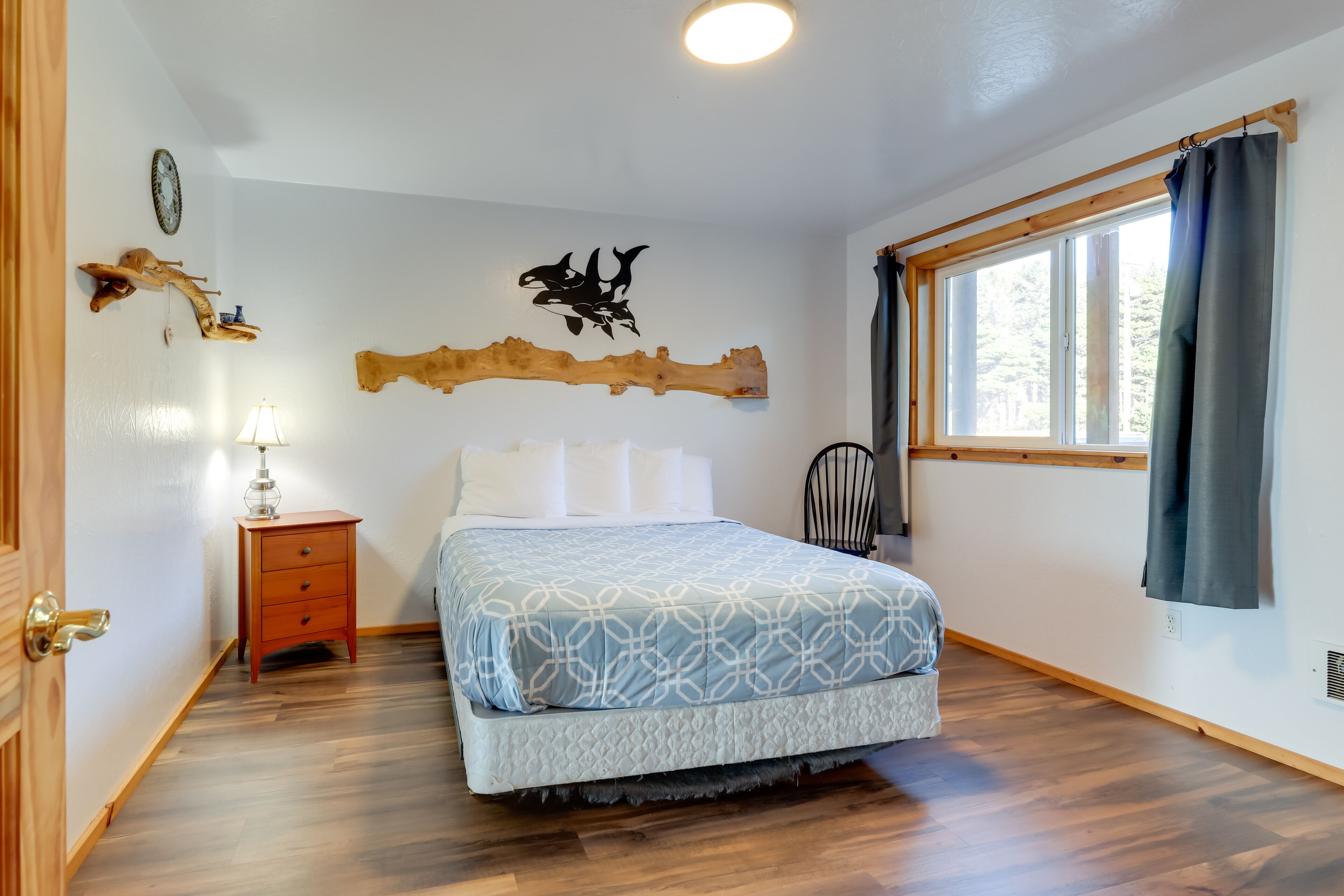 A bedroom with a bed, a nightstand, a lamp, a wall-mounted shelf, and a window with curtains.