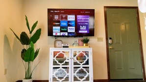 A TCL Roku TV mounted on a wall displaying various streaming services.