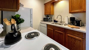 A compact kitchen with wooden cabinets, a white stove, a microwave, and a coffee maker.