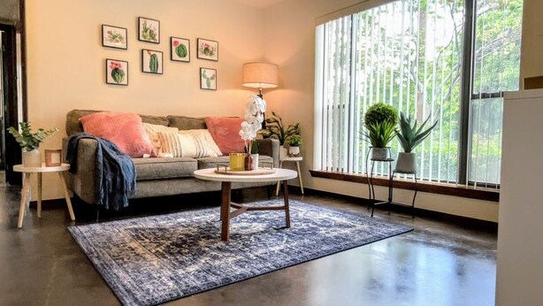 A living room with a sofa, a round coffee table, a lamp, and a large window with blinds.