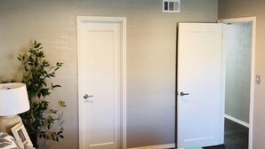 A bedroom with a bed, two doors, a plant, and a lamp.