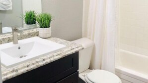 A bathroom with a white sink, black cabinets, a white toilet, a shower with a white curtain, and a small green plant on the countertop.