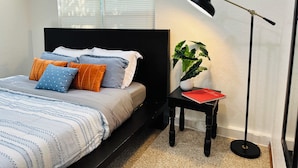 Quarto com cama, mesa de cabeceira, abajur e planta em vaso.