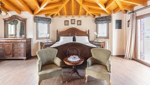 Un dormitorio con techo de madera, una cama grande, dos sillones, un aparador y una ventana con cortinas.