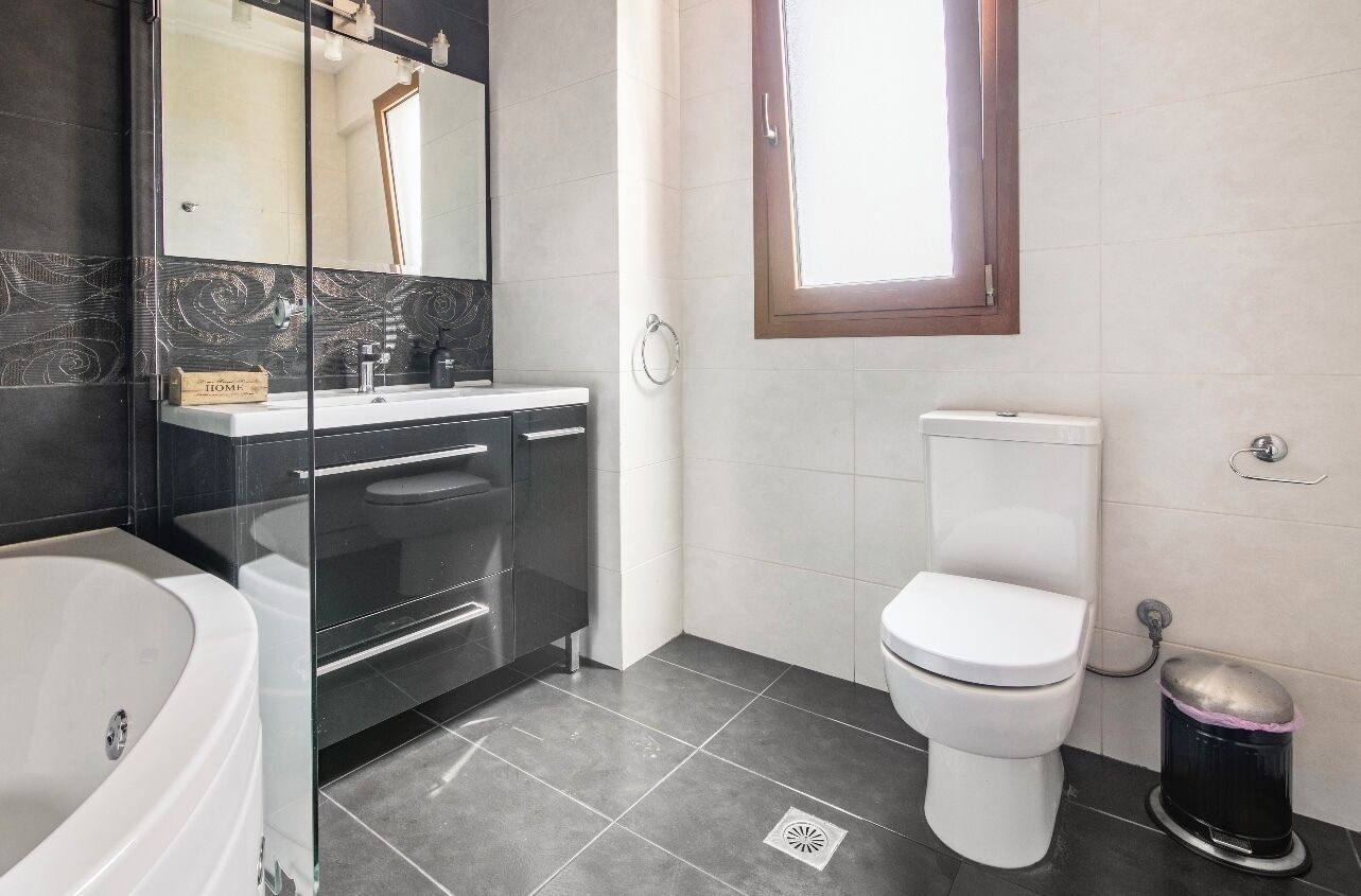 A modern bathroom with a glass-enclosed vanity, a white toilet, and a black trash bin.