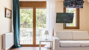 Una habitación con sofá, televisor en la pared, mesa con lámpara y vista al exterior a través de un ventanal.