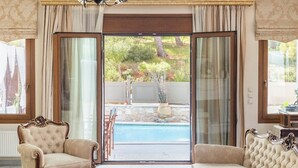 Una habitación con dos sillones ornamentados, vista a una piscina y un amplio ventanal corredero que da a un área exterior con vegetación.