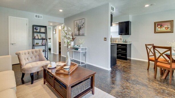 A modern living room with a sofa, coffee table, and decorative vase. There is a dining area with a table and chairs. The kitchen is visible in the background with cabinets and a countertop. - [SU 922 - 4] Graciela's Campus-close 2 bedroom luxury, Apartment near to Downtown Norman (Norman)