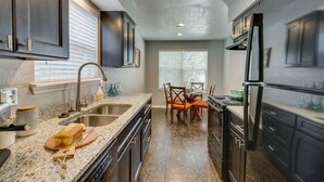 A modern kitchen with dark cabinetry, granite countertops, a built-in oven, and a dining area with orange chairs. - [SU 922 - 4] Graciela's Campus-close 2 bedroom luxury, Apartment near to Downtown Norman (Norman)