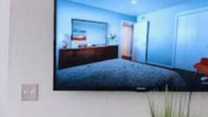 A flat-screen TV mounted on a wall displaying a bedroom with a bed, dresser, and a window. - [SU 922 - 4] Graciela's Campus-close 2 bedroom luxury, Apartment near to Downtown Norman (Norman)