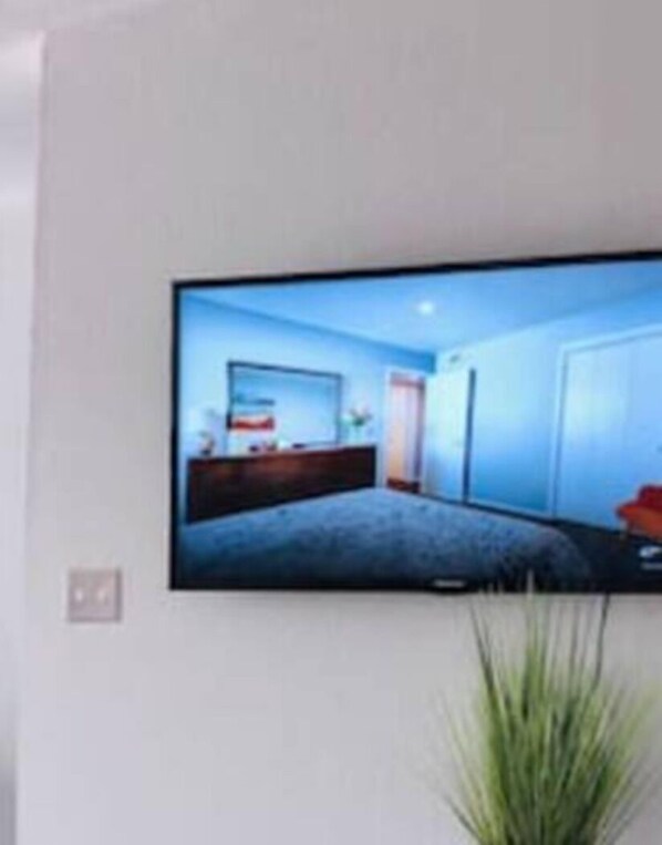 Un televisor de pantalla plana montado en la pared que muestra un dormitorio con cama, cómoda y ventana.
