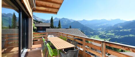 A wooden deck with a table and chairs, overlooking a mountainous landscape.