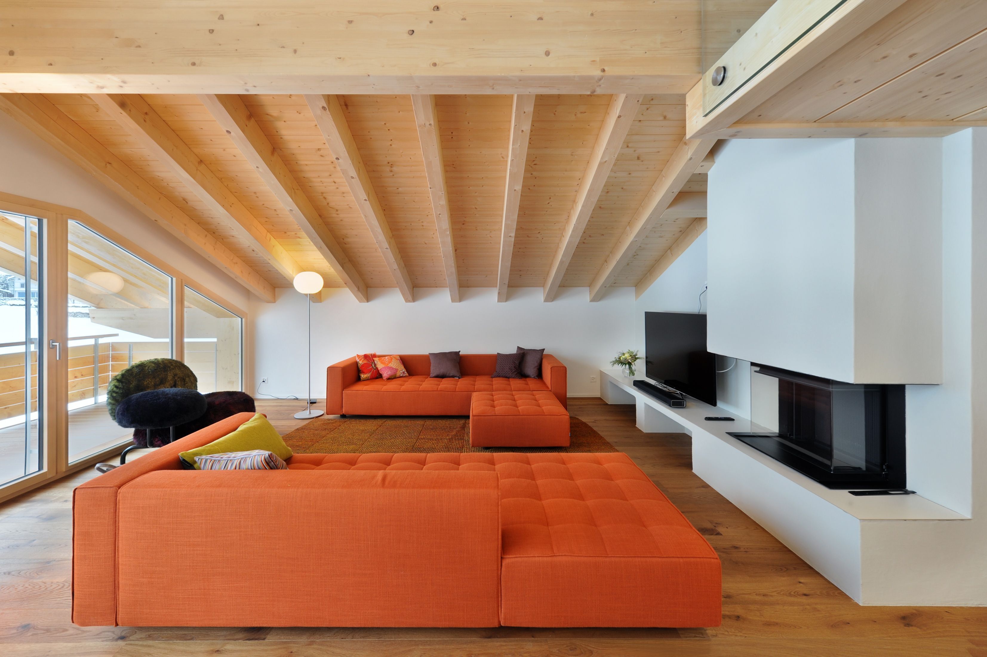 A modern living room with a large orange sectional sofa, a flat-screen TV, and a fireplace.