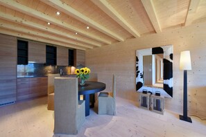 A modern interior with a wooden ceiling, a dining area with a table and chairs, and a kitchen with built-in cabinets.