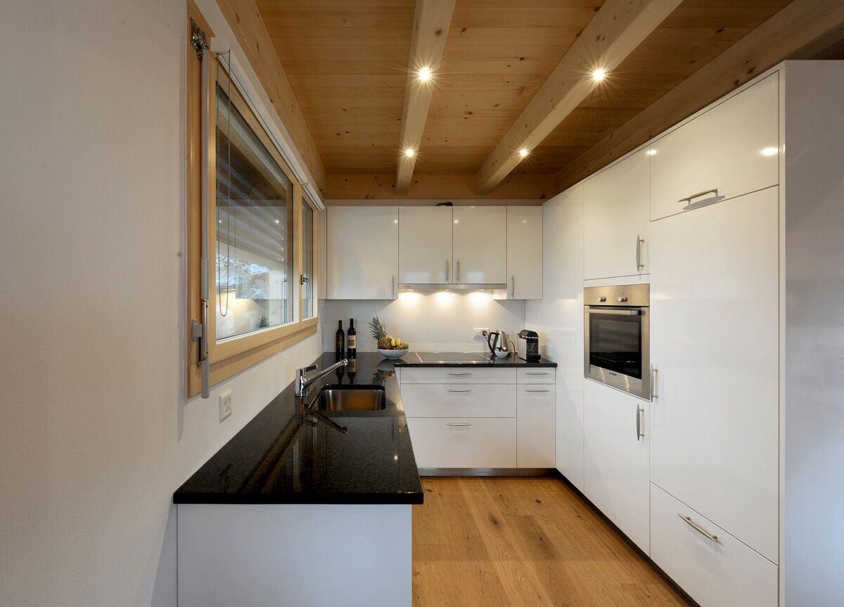 A modern kitchen with white cabinets, a black countertop, and wooden flooring.
