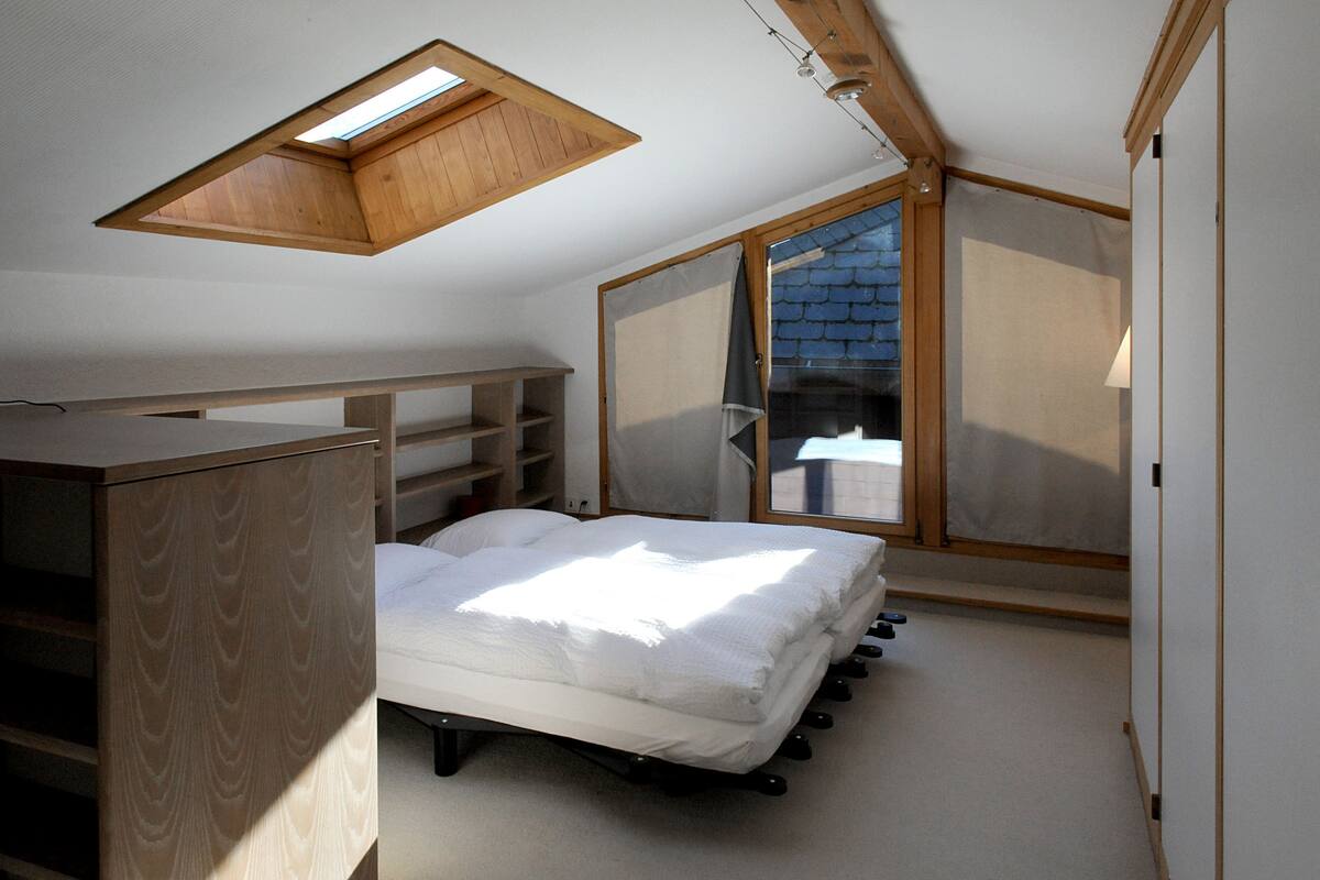 A bedroom with a skylight, a bed, a wardrobe, and a sliding door leading to a balcony.