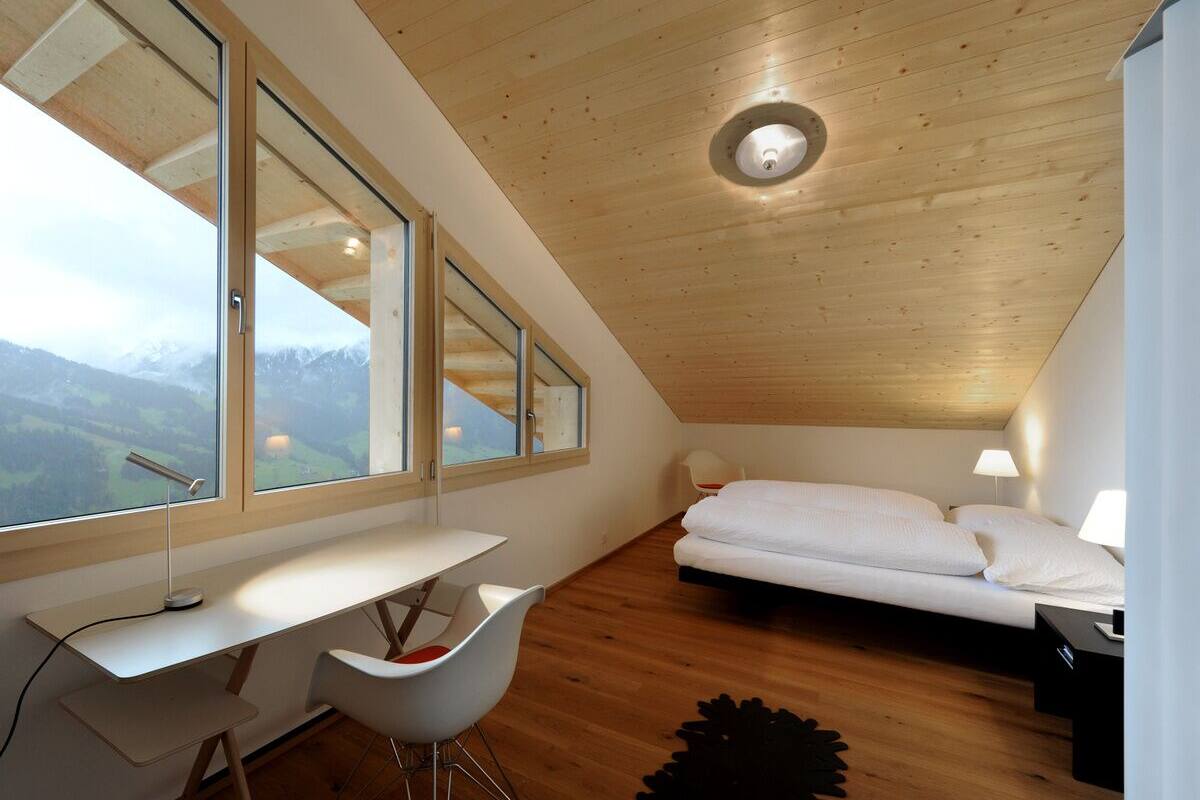 A bedroom with a wooden ceiling, a bed, a desk, and a chair.