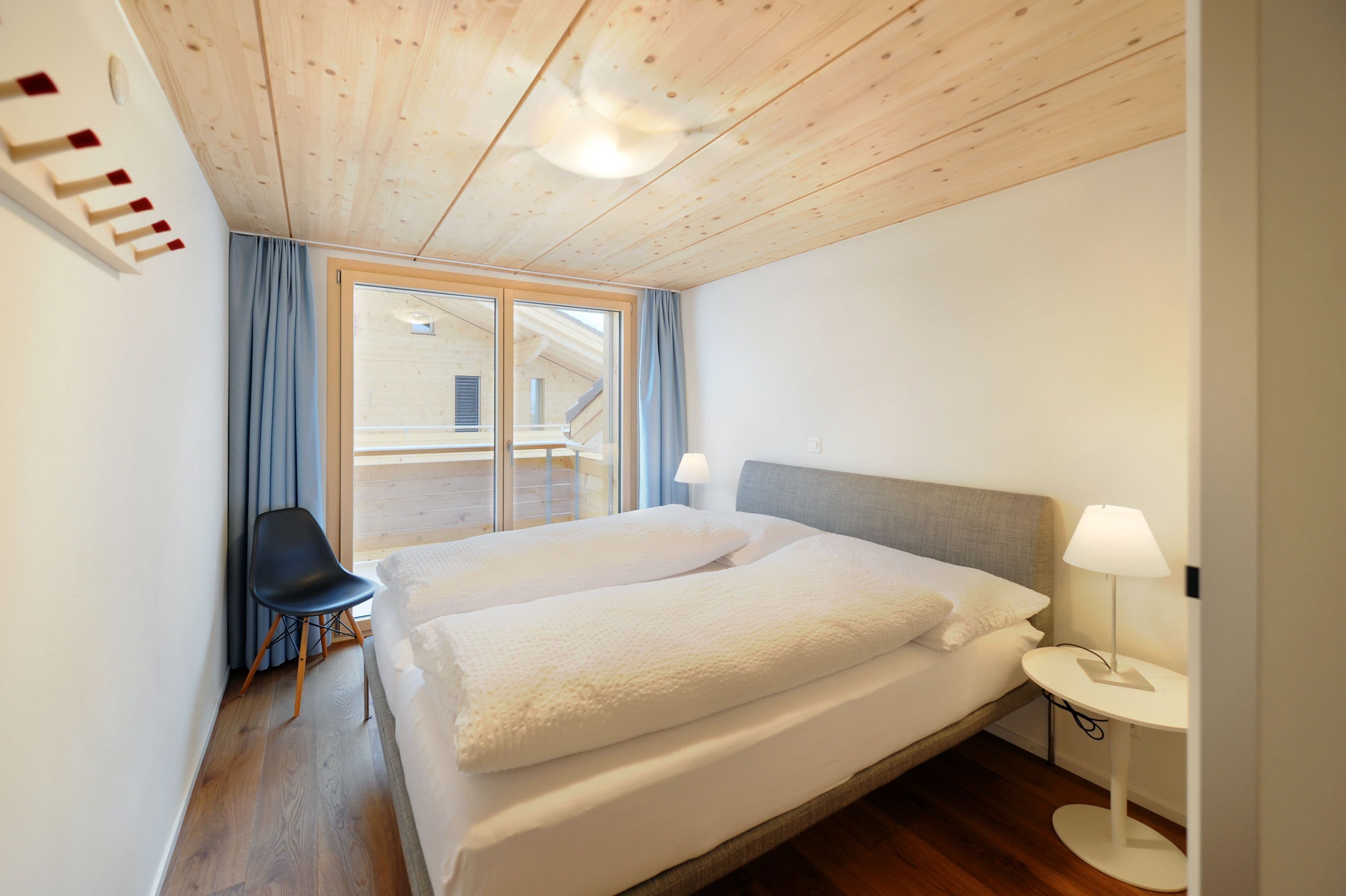 A bedroom with a large bed, a chair, a bedside table, and a view of the outside.