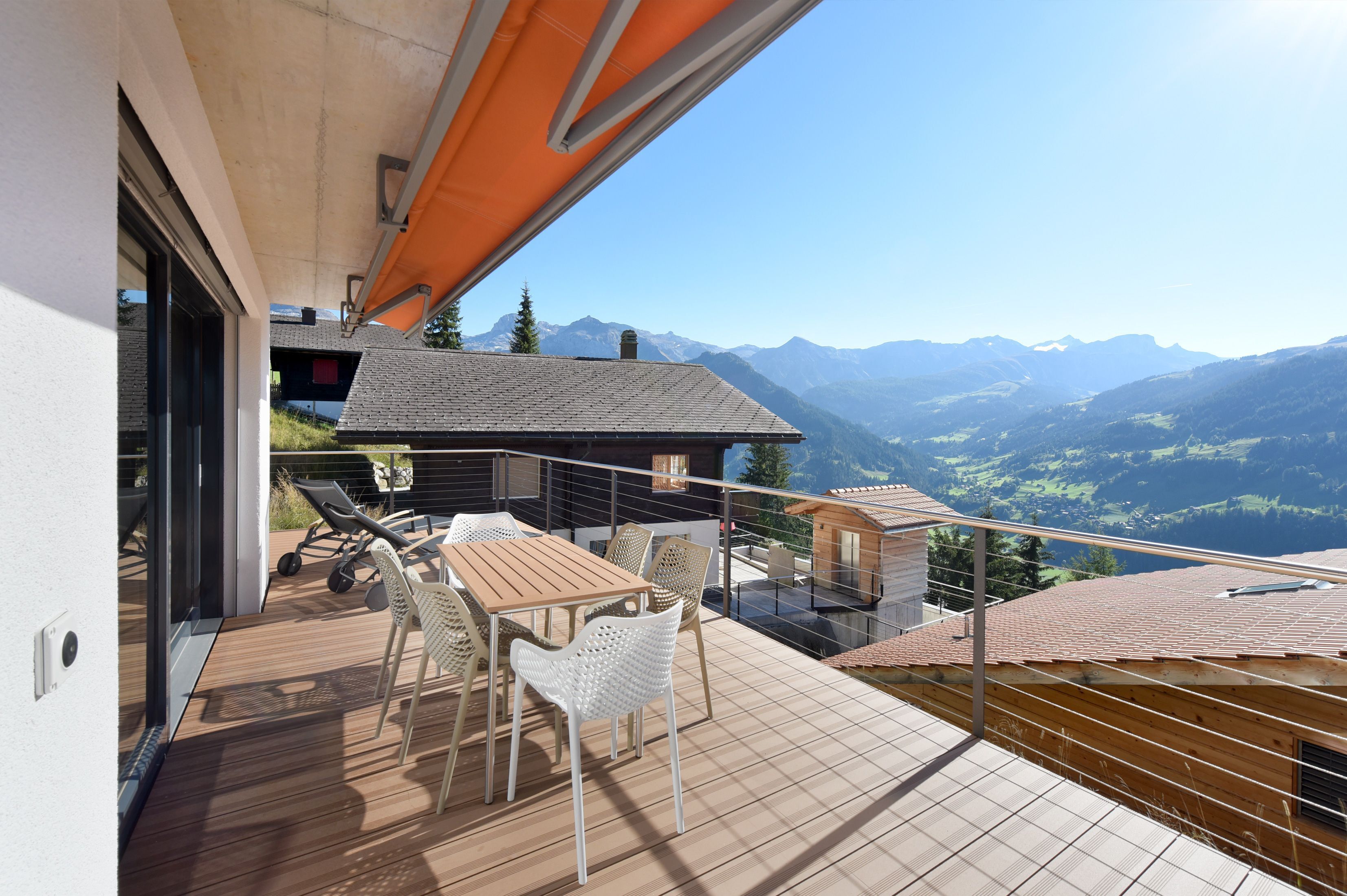 A balcony with a wooden table and chairs, overlooking a mountainous landscape.