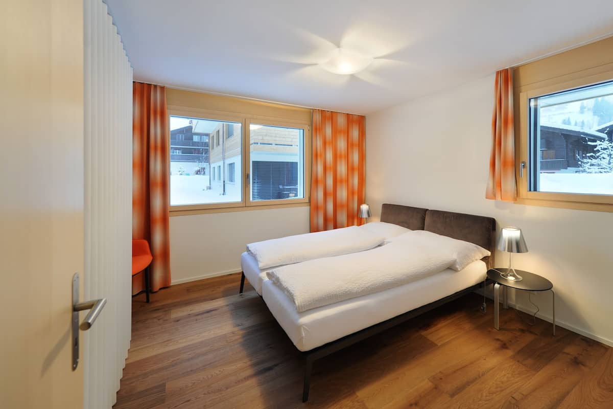 A bedroom with a bed, a nightstand, a lamp, and a window with curtains.