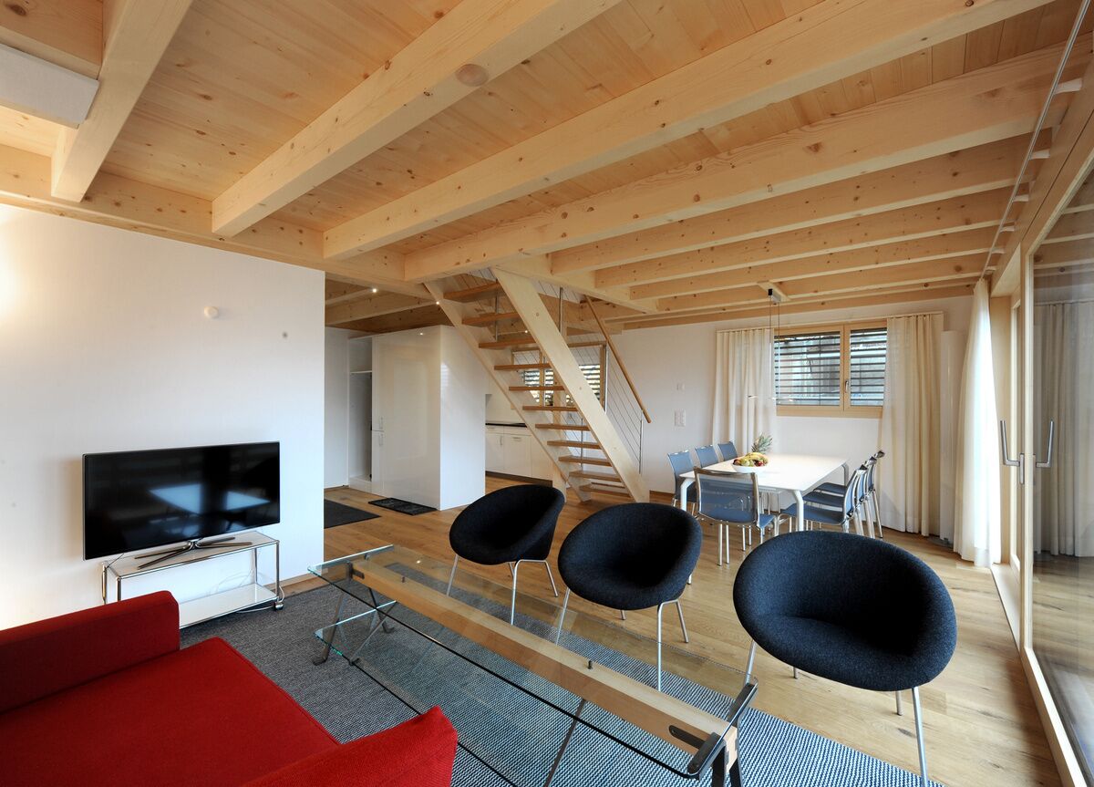 Ein modernes Interieur mit Holzboden, einem Fernseher auf einem Schrank, einem roten Sofa und einem Essbereich mit Stühlen und einem Tisch.