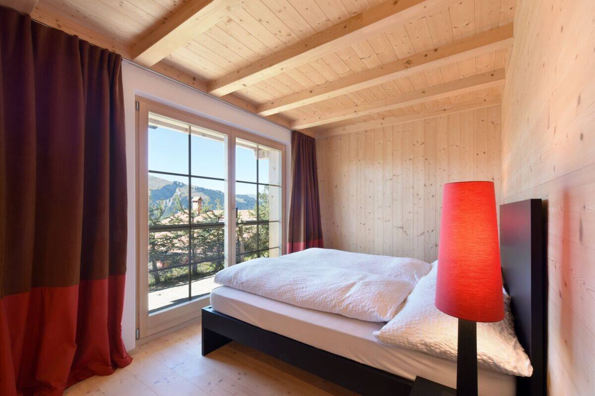 A bedroom with a bed, a window with curtains, and a view of the outdoors.