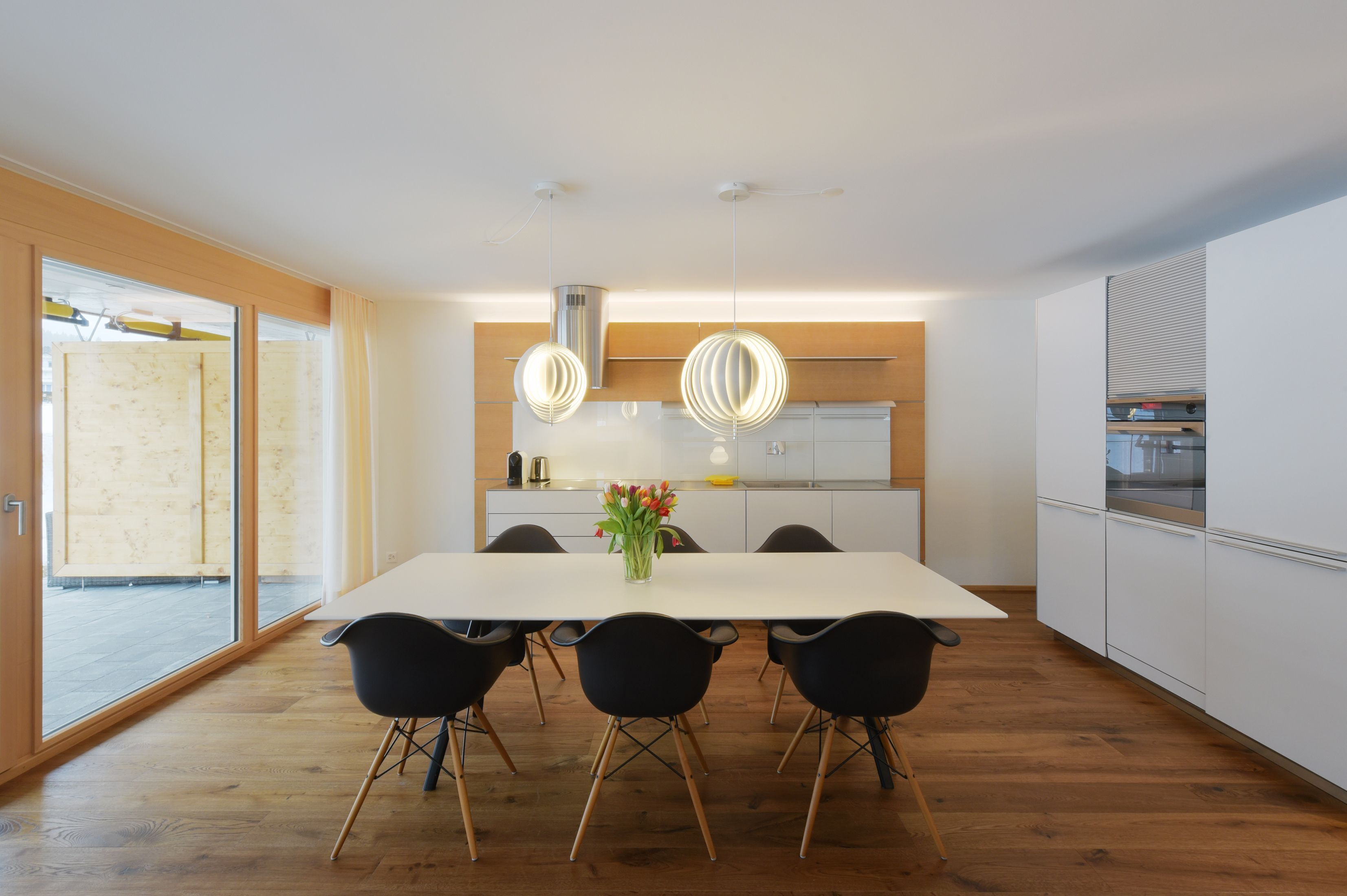 A modern kitchen with a large dining table, black chairs, and pendant lights.