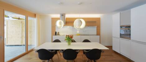A modern kitchen with a large dining table, black chairs, and pendant lights.