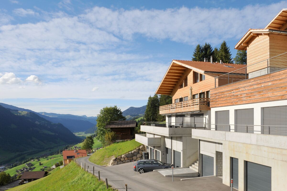 A modern two-story building with a wooden facade, a balcony, and a car parked in front.