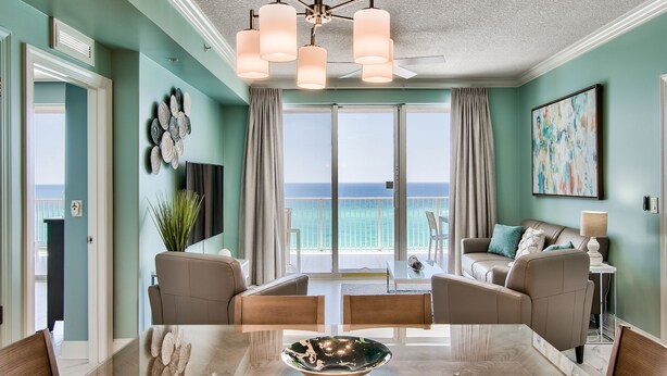 Un salón amplio con un gran ventanal que da a un balcón, un comedor con mesa de vidrio, y vista al océano.