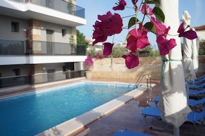 A swimming pool with a clear blue water, surrounded by lounge chairs and a white umbrella. - Vellum Hotel (Kassandra)