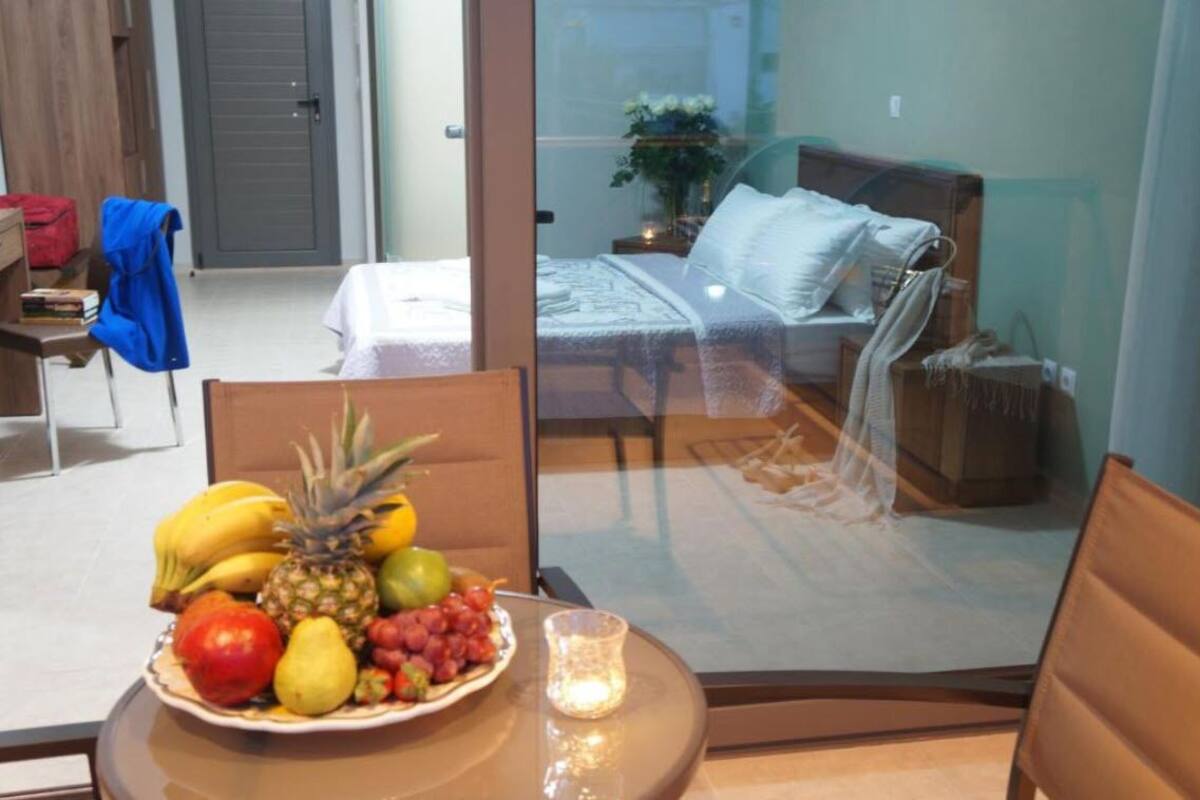 Une chambre d’hôtel comprenant un lit, une table de chevet avec un panier de fruits, une chaise et une cloison en verre.