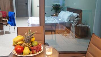 Ein Hotelzimmer mit einem Bett, einem Nachttisch mit Obstschale, einem Sessel und einer Glastrennwand.