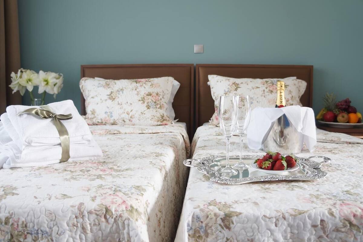 Deux lits avec une literie à motifs floraux, un plateau avec des fraises, une bouteille de champagne et un vase rempli de fleurs.