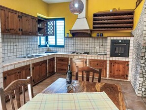 Een keuken met houten kastjes, een betegelde achterwand, een inbouwoven en een eethoek met een tafel en stoelen.