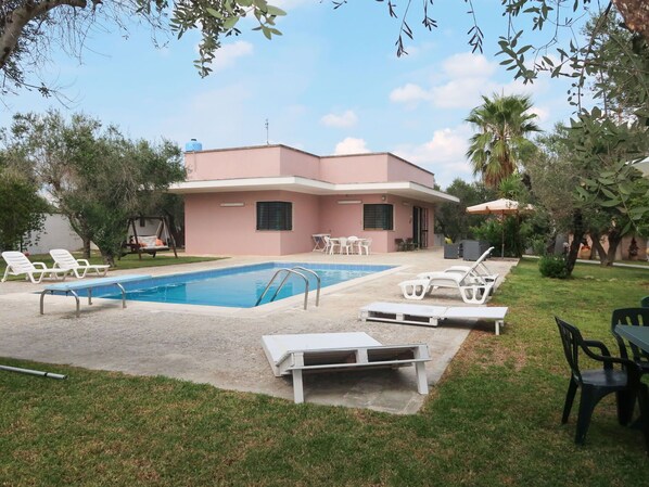 A pink building with a swimming pool, surrounded by grass and trees.