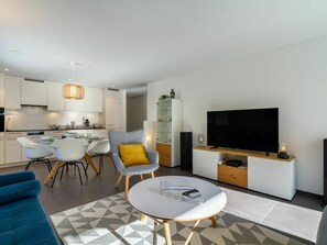 A modern living room with a TV, seating, and a kitchen in the background. - Cosy apartment for 4 people with WIFI, TV, terrace and panoramic view (Kandersteg)