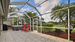 Un patio cubierto con vista a un campo de golf, sillas rojas y un jacuzzi.