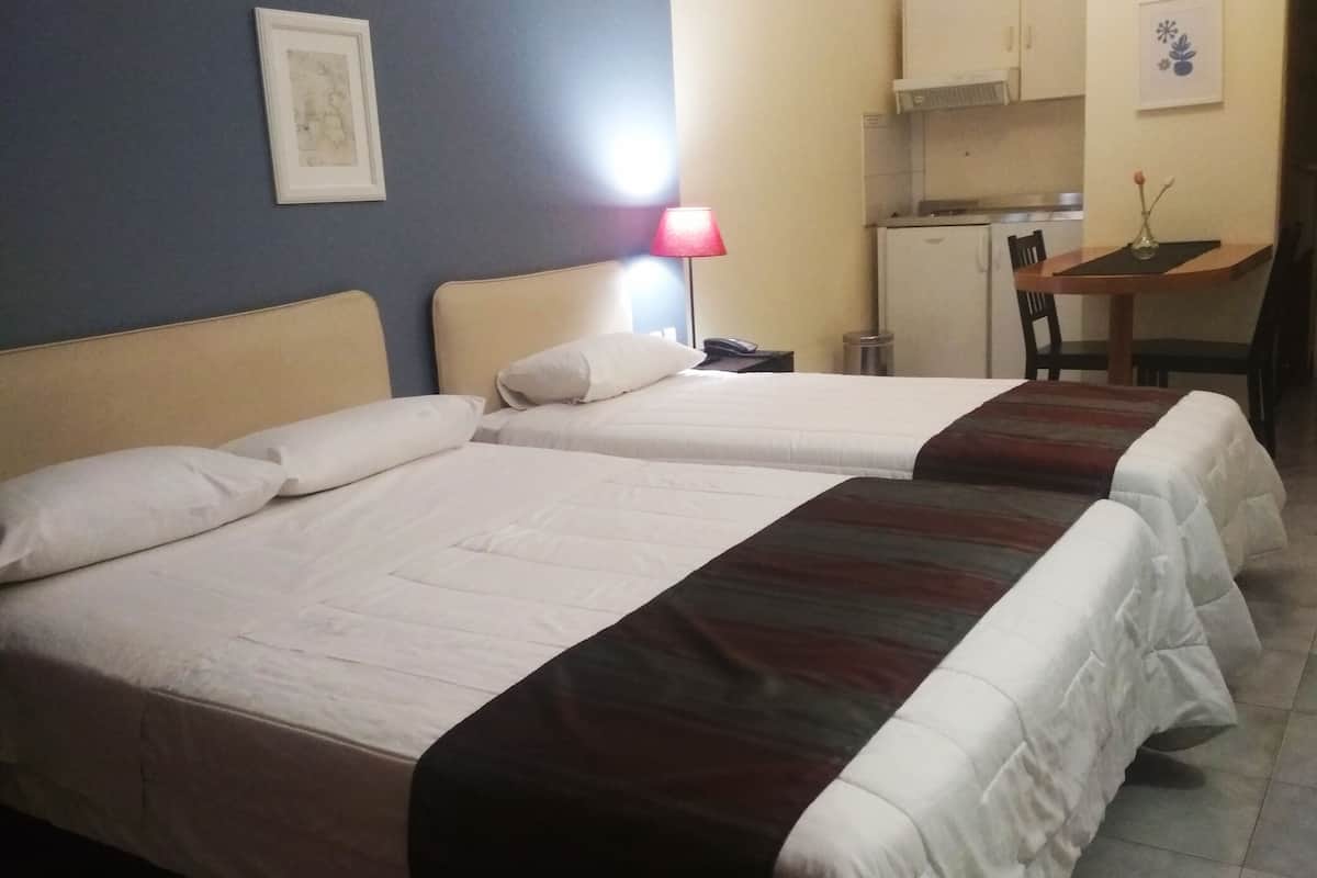 A hotel room with two beds, a desk, and a kitchenette.