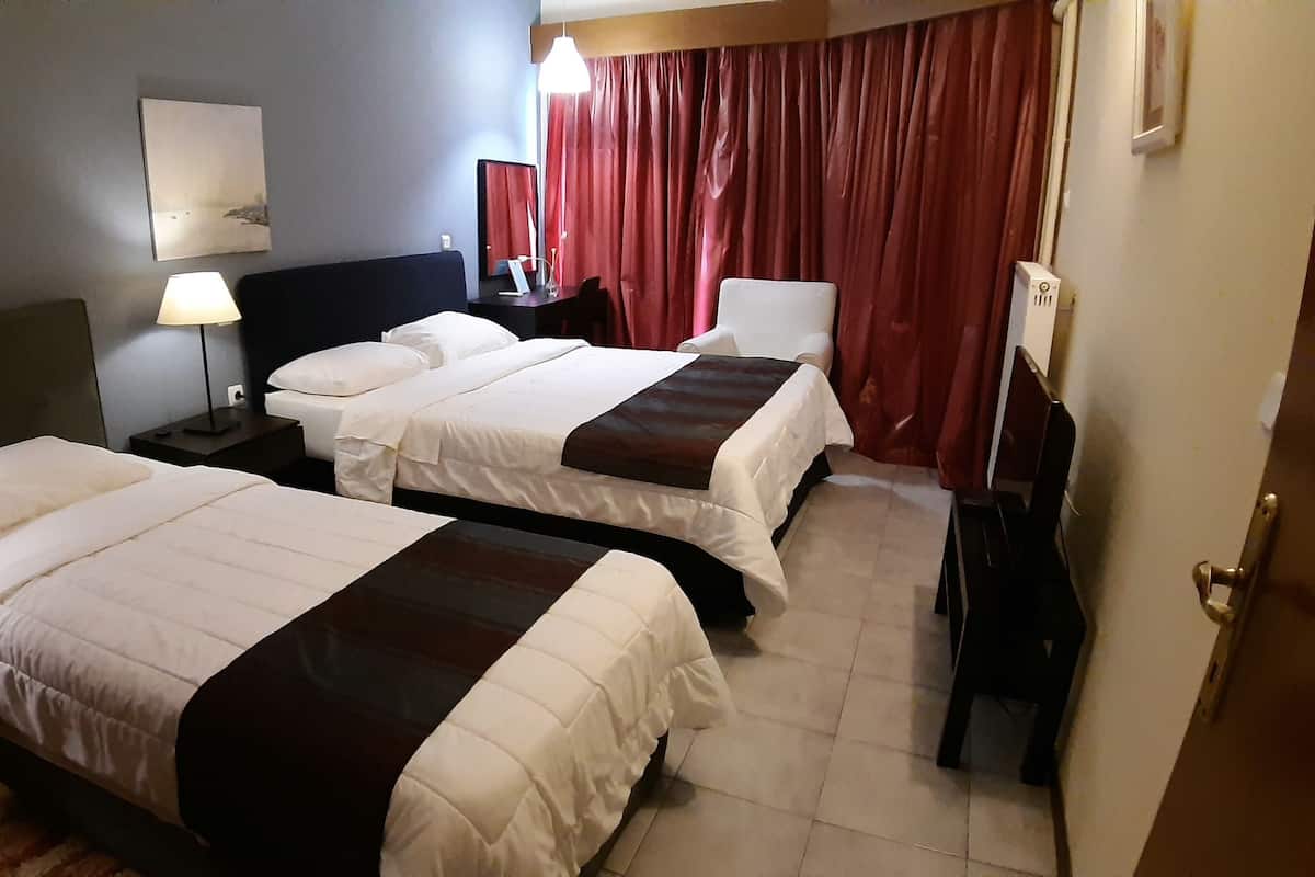 A hotel room with two beds, a desk, a chair, a lamp, and a TV.