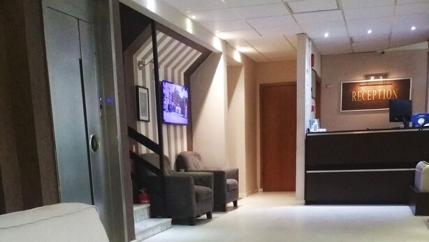 Un espace d’accueil comprenant un comptoir de réception, un téléviseur fixé au mur et un escalier menant à un autre étage.