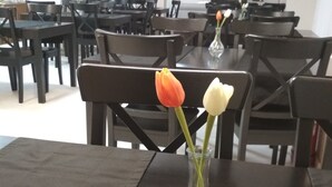 Un espace repas avec des tables et des chaises, et un vase rempli de fleurs posé sur l’une des tables.