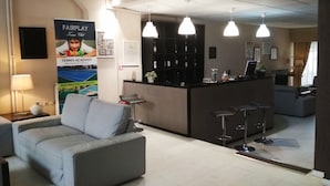 Un hall d’hôtel moderne avec un canapé gris, un comptoir d’accueil et un espace bar.