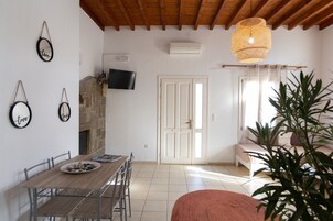 Un comedor con una mesa y sillas de madera, una chimenea de piedra, un televisor montado en la pared y un ventanal con cortinas.
